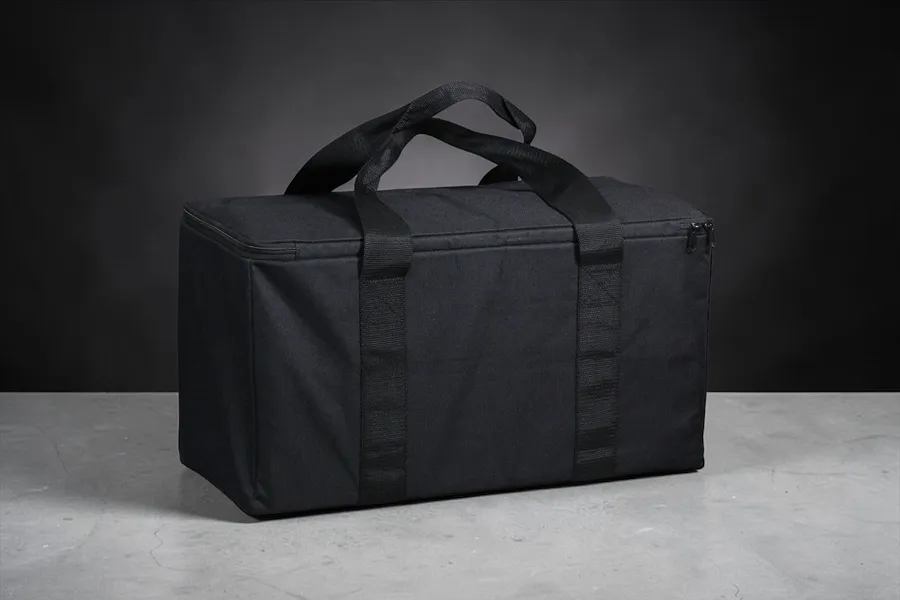 A black rectangular RC storage bag with carry handles, sitting on a grey concrete surface against a dark background.