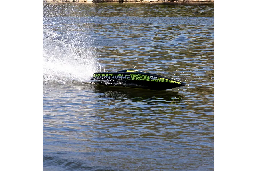 A black Pro Boat Sonicwake V3 RC speed boat racing across the water, creating a large splash behind it.