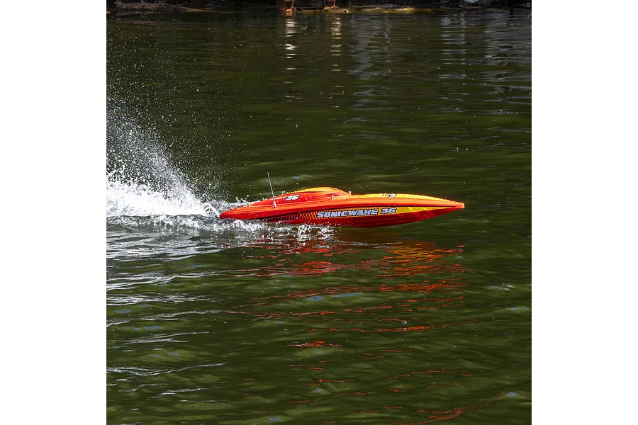 A red Pro Boat Sonicwake 36 RC speed boat racing across dark water, creating a spray behind it.