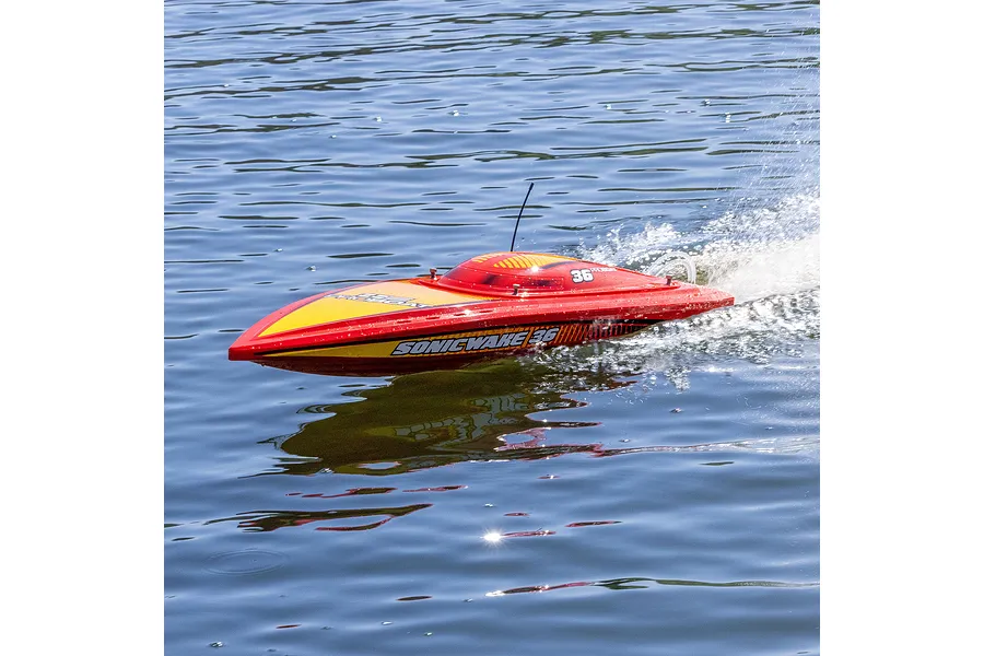 A red and yellow Pro Boat Sonicwake 36 RC speed boat racing across blue water, creating a wake behind it.