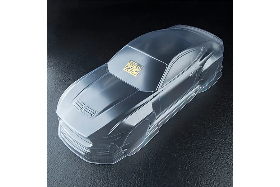 A clear, unpainted 1/10 scale RC car body shell, viewed from a high angle against a dark, textured background.