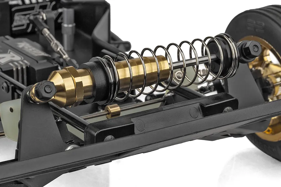 Close-up of the gold-anodized shock absorber and suspension assembly on a Team Associated RC10 buggy chassis.