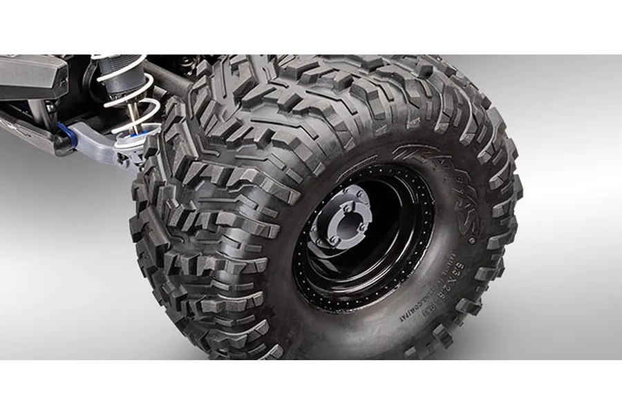 Close-up of a Traxxas RC monster truck wheel and suspension assembly on a grey background.