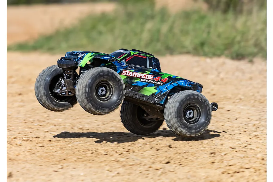 A Traxxas Stampede 4X4 VXL brushless RC monster truck performing a jump on a dirt track.