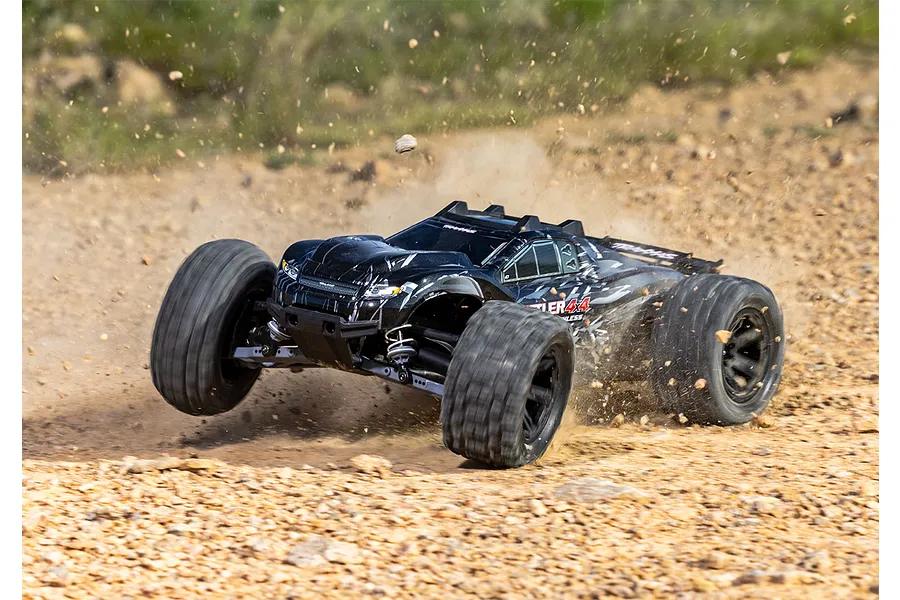 A black Traxxas Rustler 4X4 RC stadium truck driving fast over a dirt track, kicking up dust and gravel.