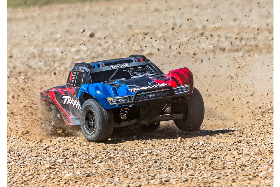 A Traxxas Slash 4X4 RC short course truck driving fast on a gravel track, kicking up dirt and rocks.