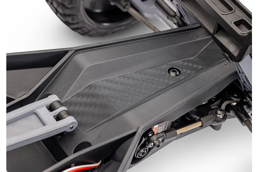 Close-up of the black composite chassis and steering assembly of a Traxxas RC vehicle, showing the carbon fiber pattern detail.