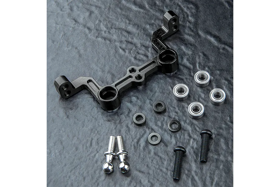 MST black aluminium steering joint plate with included bearings, screws, and spacers on a dark textured surface.