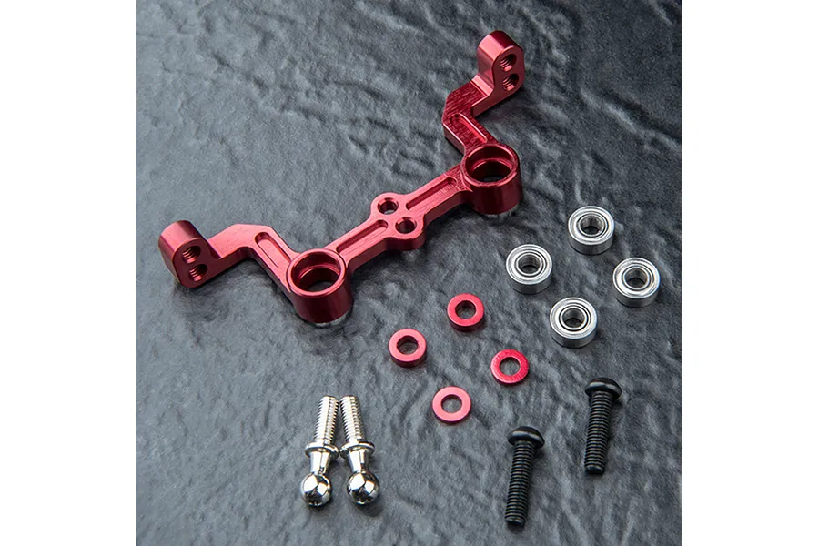 MST red anodized aluminium steering joint plate with included bearings, spacers, and screws on a dark textured surface.