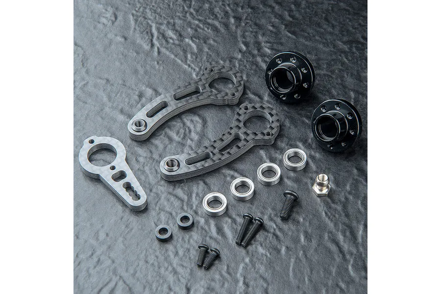 MST carbon fibre steering arm set with black metal hubs, bearings, and screws laid out on a textured black surface.