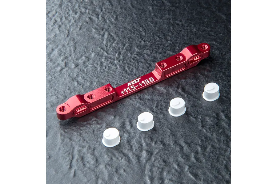A red anodized aluminium MST adjustable lower suspension arm mount with four small white plastic bushings on a textured black surface.