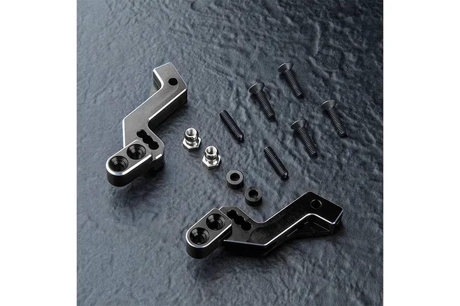 A pair of black MST aluminium rear shock braces with included screws, nuts, and spacers on a dark textured surface.