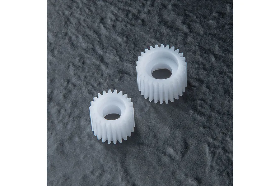 Two white plastic idler gears of different sizes resting on a dark textured surface.