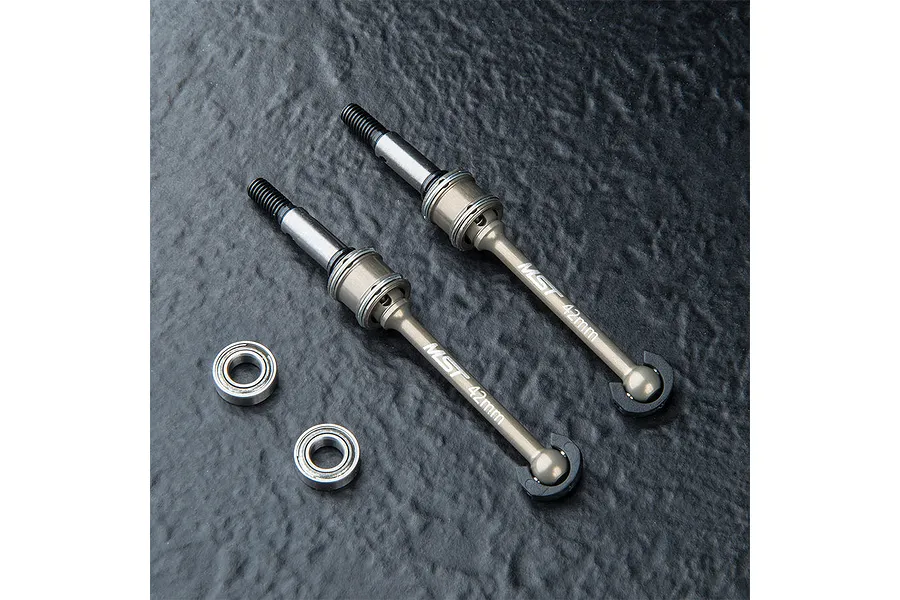 Two MST 42mm lightweight aluminium CVD driveshafts and two ball bearings on a dark textured surface.