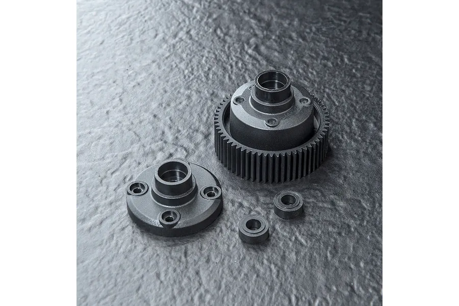 MST bevel gear differential set components including a large gear housing, a circular cover plate, and two small ball bearings on a dark textured surface.