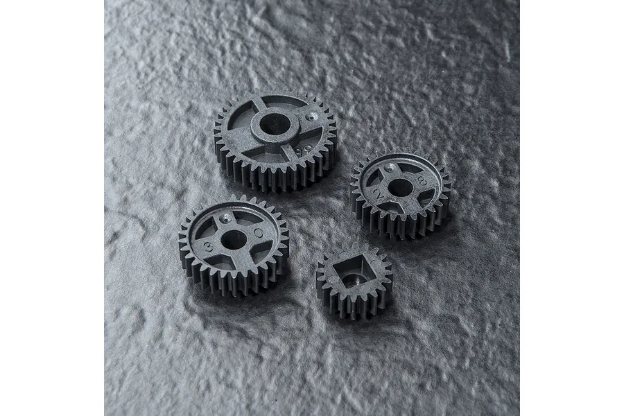 A set of four grey plastic RC drive gears of varying sizes arranged on a dark textured surface.