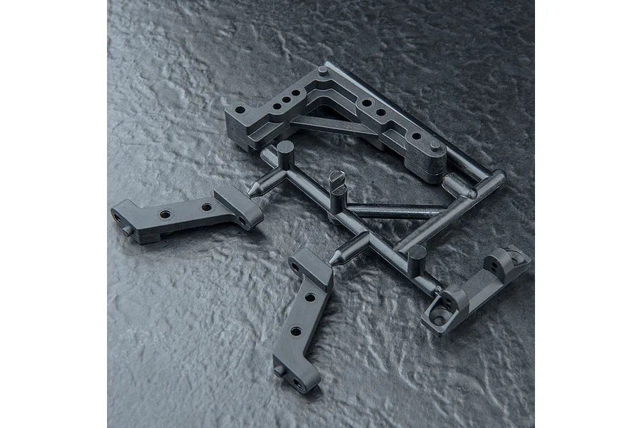 A black plastic parts tree containing various RC chassis fittings and suspension mounts on a textured dark surface.