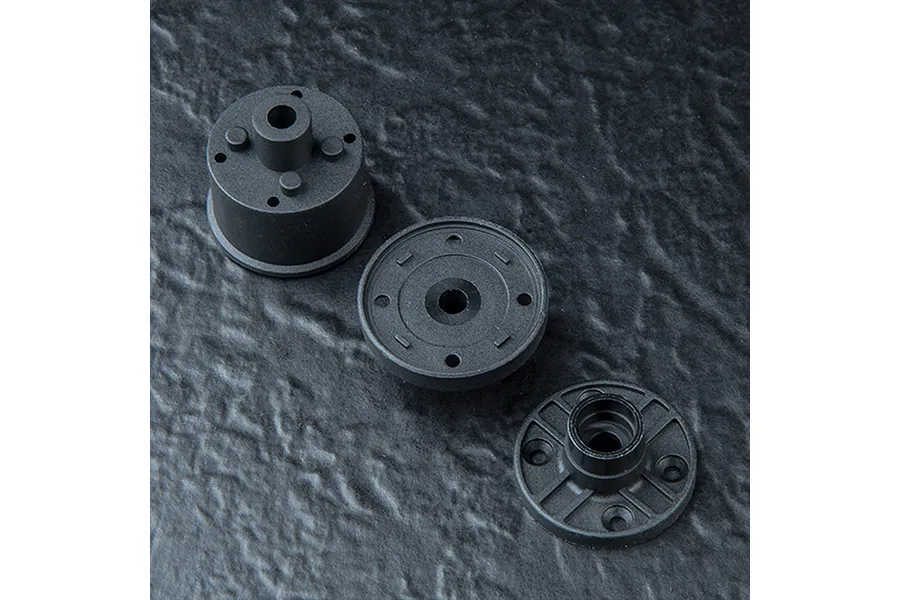 Three black plastic RC gearbox components arranged on a textured dark grey surface.