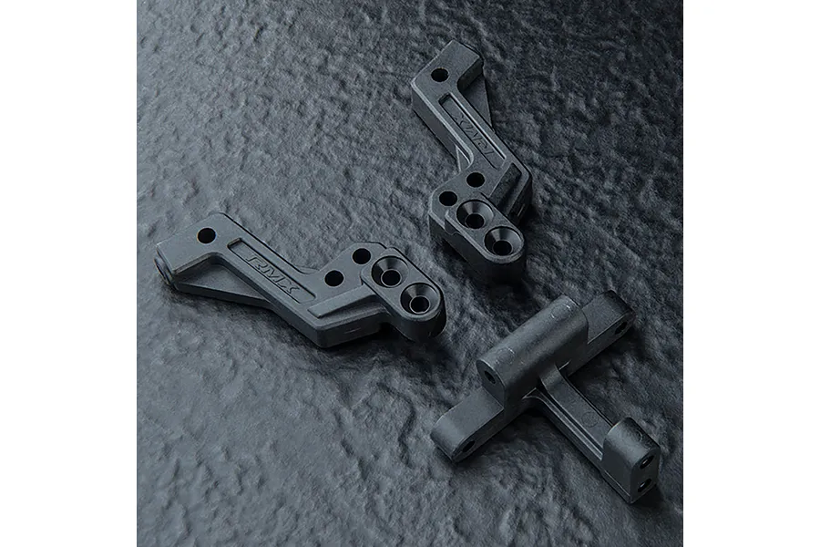 MST RMX series black plastic rear shock mount and gearbox connector parts on a textured dark background.