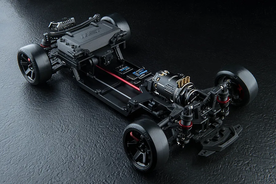 High-angle studio shot of an MST FRX S 1/10 scale RC drift car chassis, showing the front-motor layout and black plastic components on a dark textured surface.
