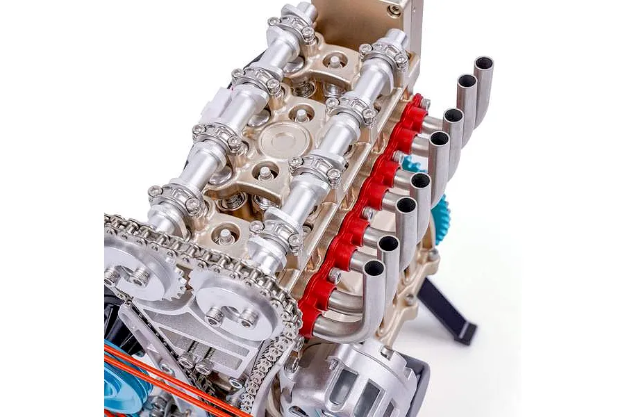 Close-up view of the Teching DM113 four-cylinder engine model kit, showing the camshafts, exhaust manifold, and timing chain assembly.