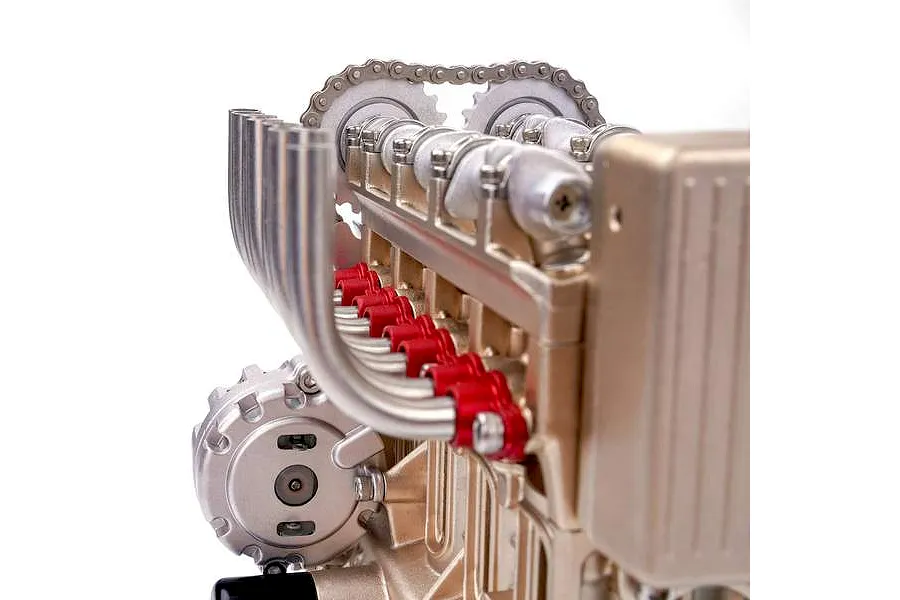 Close-up of the Teching DM113 four-cylinder engine model kit showing metal components, red accents, and a timing chain mechanism.