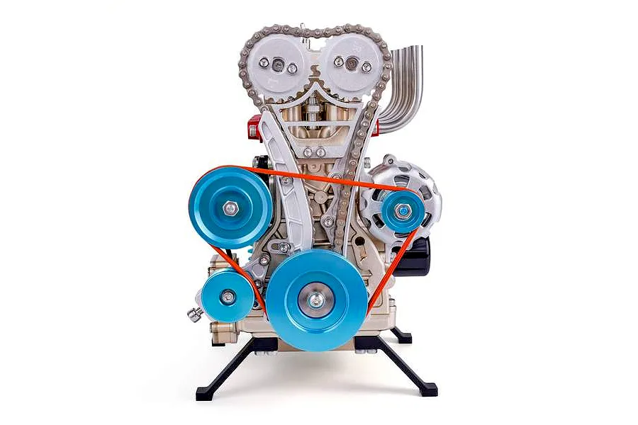 A front view of the Teching DM113 four-cylinder engine model kit, showing metallic components, blue pulleys, and a timing chain on a white background.