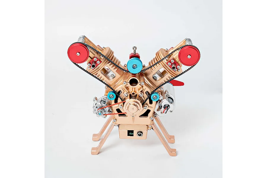A front view of the Teching M114 V2 engine model kit, featuring a gold-colored metal frame, red pulleys, and blue accents against a white background.