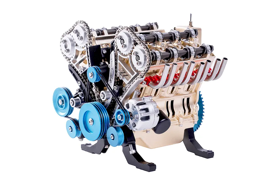 A detailed metal model of a V8 engine with gold, blue, and silver components, featuring visible timing chains, pulleys, and exhaust headers.