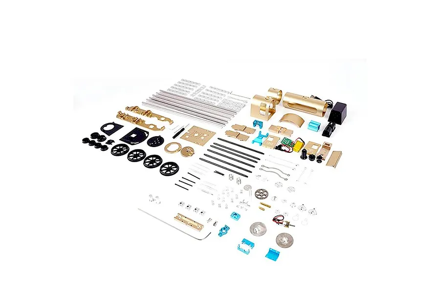 An exploded view of the Teching DM221 steam train model kit showing various metal parts, wheels, rods, and electronic components laid out on a white background.