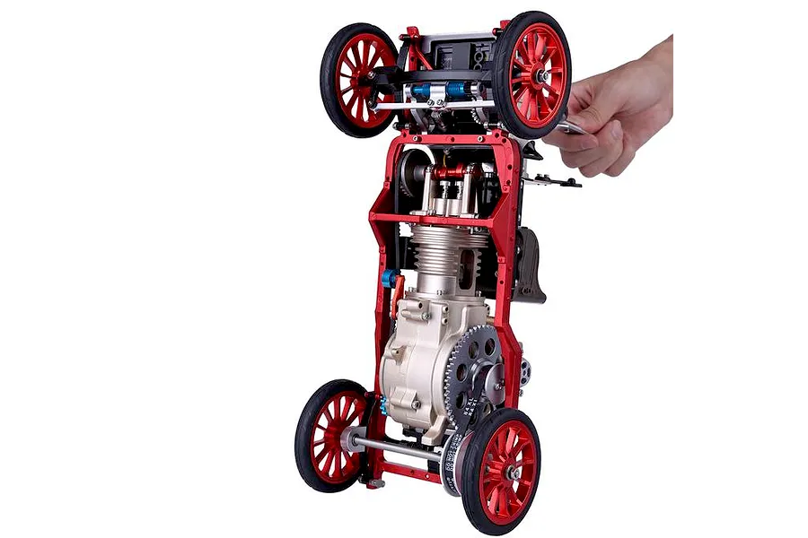 A hand holding a partially assembled Teching DM227 classic car model kit, showing the metal chassis, engine block, and red spoked wheels.