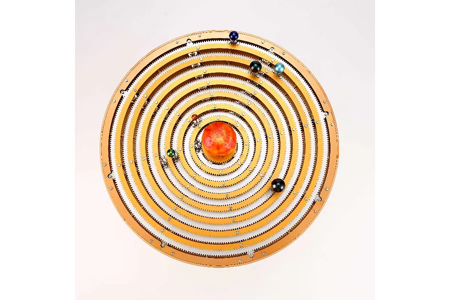 Top-down view of a Teching DM405 solar system metal model kit featuring concentric golden gear rings and colorful planet spheres around a central sun.