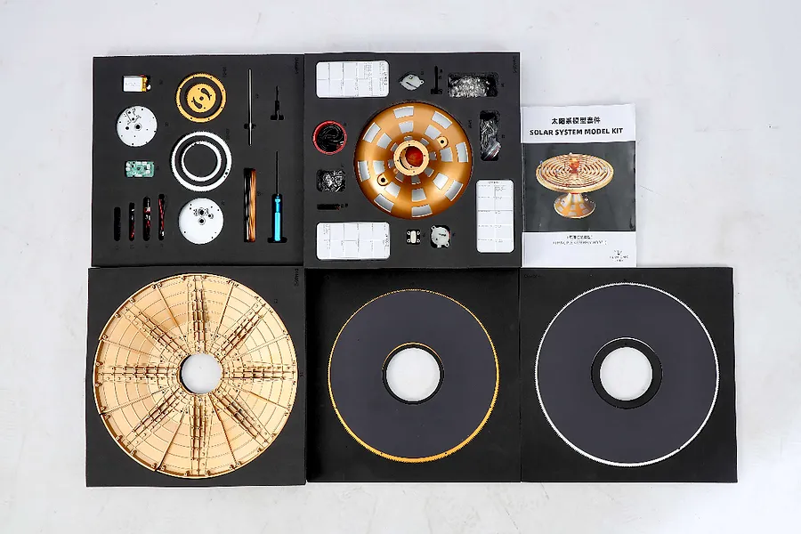 Top-down view of the Teching DM405 Solar System model kit components laid out in foam trays with an instruction manual.