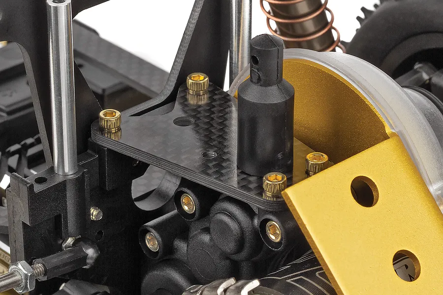 Close-up of the carbon fiber shock tower and gold anodized motor plate on a Team Associated RC10 buggy.