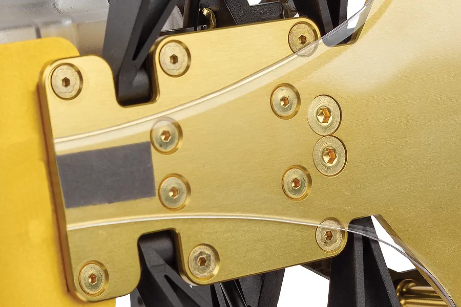 Close-up of the gold-anodized aluminum chassis plate and black plastic components of a Team Associated RC10 buggy.