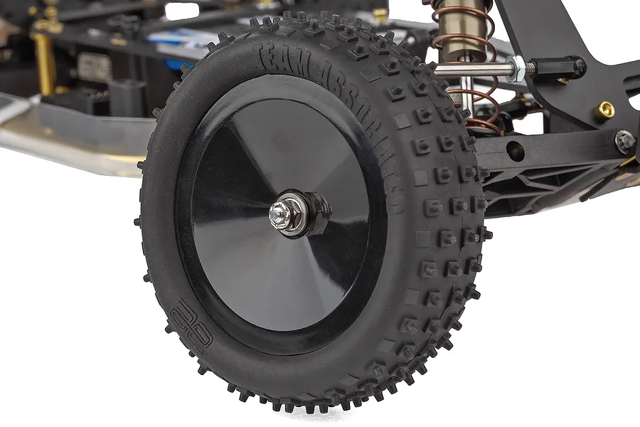 Close-up of the front wheel and suspension of a Team Associated RC10 buggy, showing a black dish wheel with knobby rubber tire.