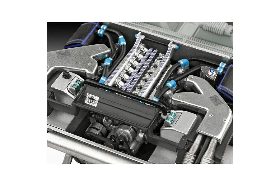 Close-up of a detailed scale model car engine, showing metallic components, black hoses with blue connectors, and small decals.
