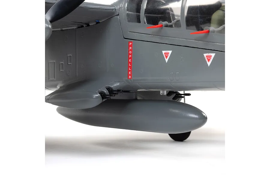 Close-up of the fuselage of an E-Flite Micro OV-10 Bronco RC plane, showing grey paint, propeller warning labels, and ejection seat markings.