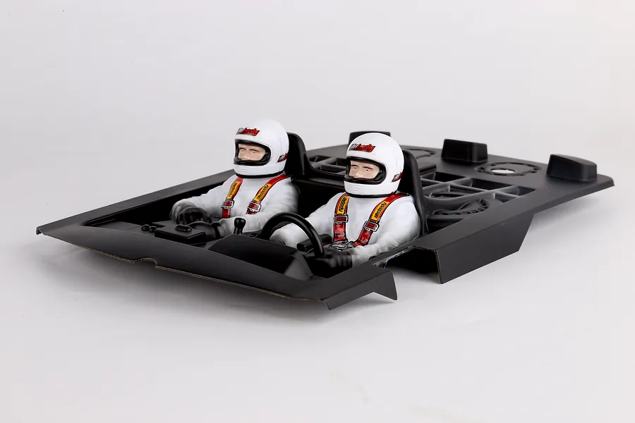 Killerbody Lancia Stratos Gr.4 painted RC cockpit interior with two driver figures in white racing suits and helmets, set in a black plastic tray.