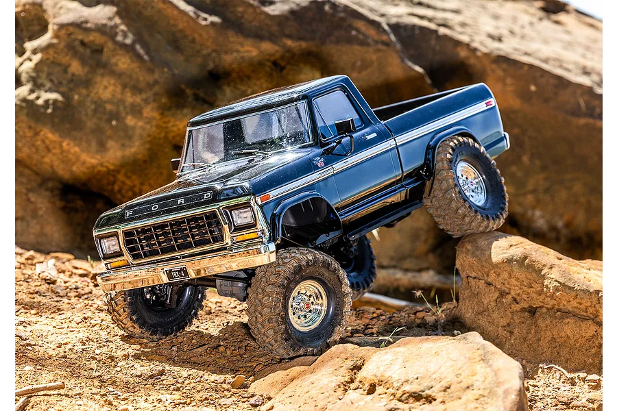 A black Traxxas TRX-4 1979 Ford F-150 Ranger XLT RC rock crawler driving over rugged rocky terrain outdoors.