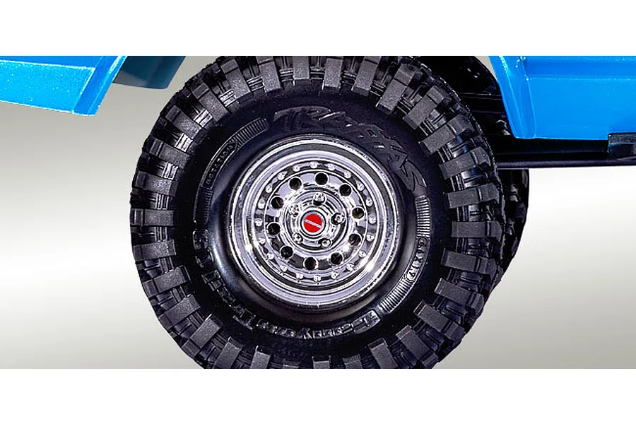 Close-up of a Traxxas RC crawler wheel with a chrome rim and black off-road tire, positioned under a blue vehicle body.