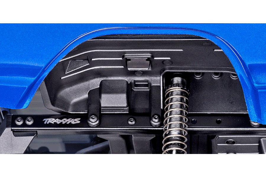 Close-up of the wheel well and suspension of a Traxxas TRX-4 RC crawler, showing the blue body, black inner fender, and coil-over shock absorber.
