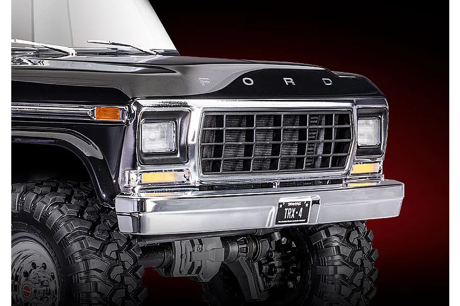 Close-up of the front grille, bumper, and hood of a black Traxxas TRX-4 1979 Ford F-150 RC crawler against a dark red background.