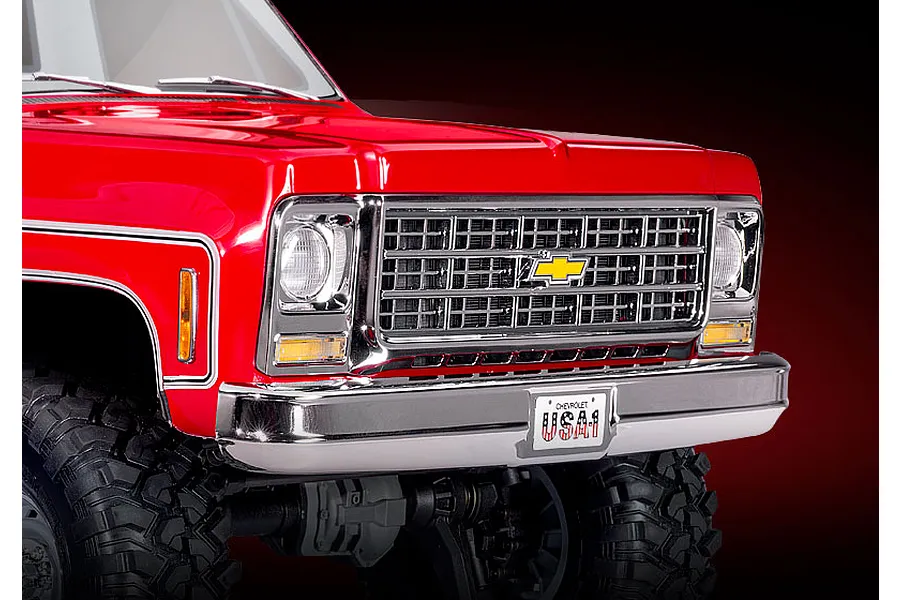 Close-up of the front end of a red Traxxas TRX-4 1979 Chevrolet Cheyenne K10 RC crawler, showing the chrome grille, headlights, and USA-1 license plate.