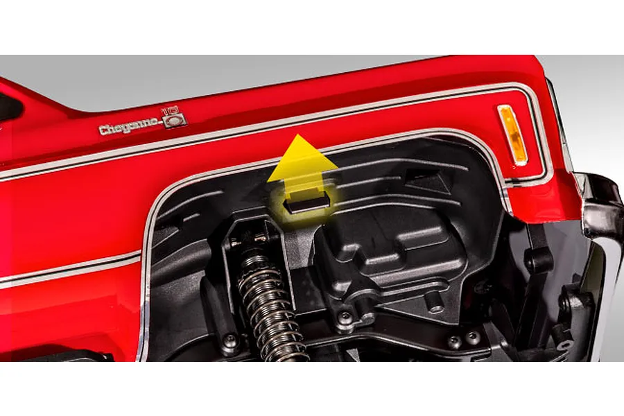 Close-up of the Traxxas TRX-4 Chevrolet K10 wheel well showing the body mounting clip location with a yellow arrow indicator.