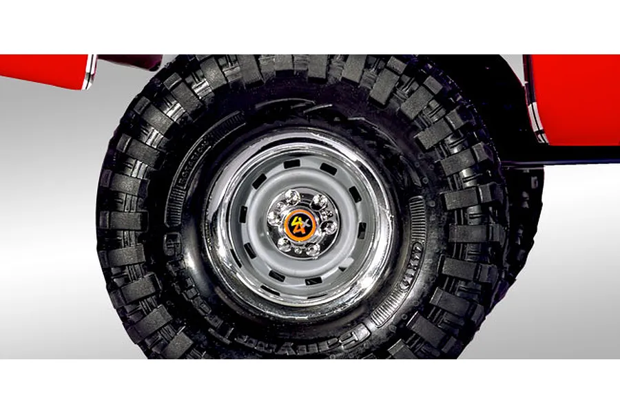 Close-up of a Traxxas TRX-4 RC crawler wheel featuring a chrome steel-style rim with a 4x4 center cap and aggressive tread pattern.