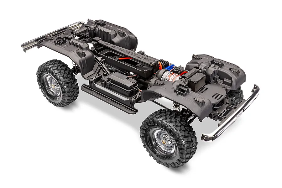 A high-angle studio shot of a Traxxas TRX-4 RC crawler chassis without the body shell, showing the frame, wheels, motor, and drivetrain components.