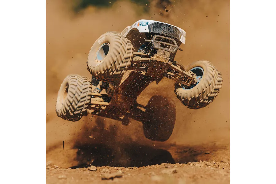 An ARRMA RC monster truck mid-air, kicking up dirt and dust while performing a jump on a dirt track.