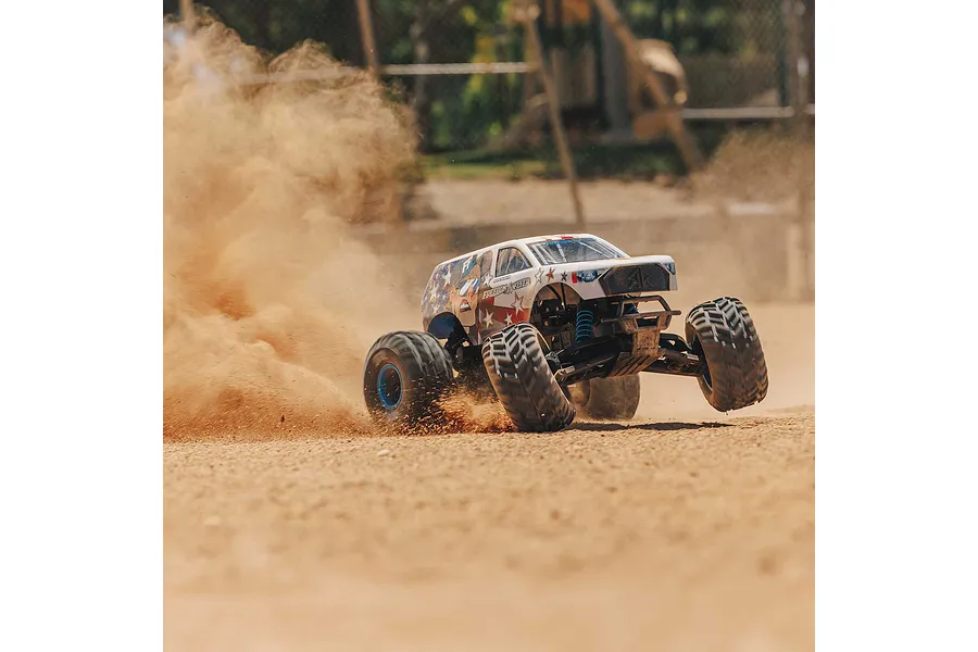 An ARRMA Freedom Flyer RC monster truck kicking up a large cloud of dust while driving on a dirt track.