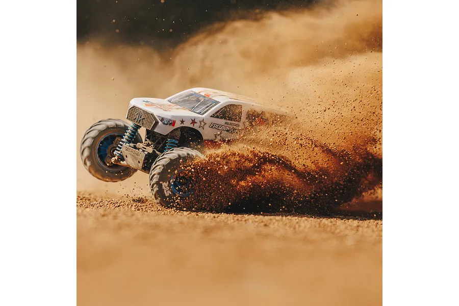 ARRMA Freedom Flyer Grom RC monster truck drifting on a dirt track, kicking up a large cloud of dust.